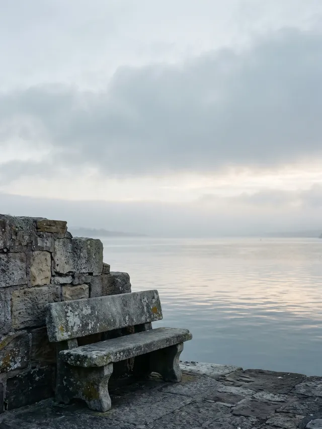 A bare stone bench by a harbour at dawn